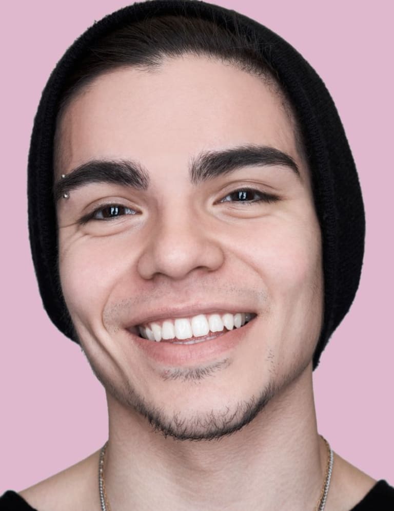 A Young man with an eyebrow piercing and a beanie smiling.