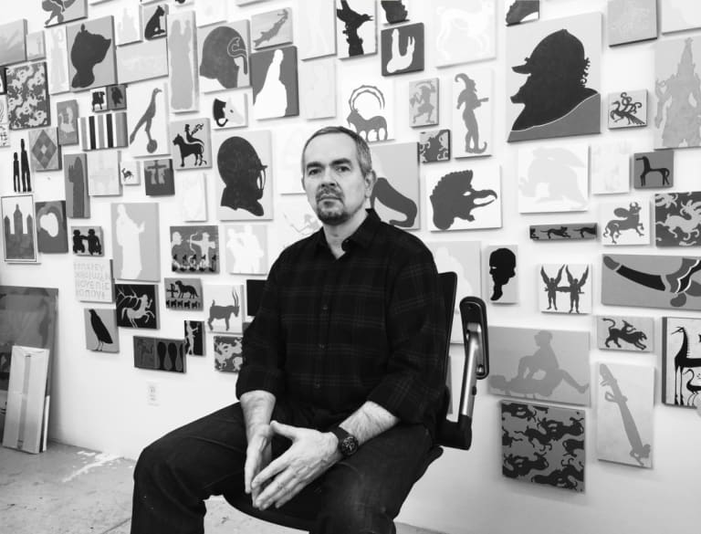 Man sitting in front of various pieces of art work.