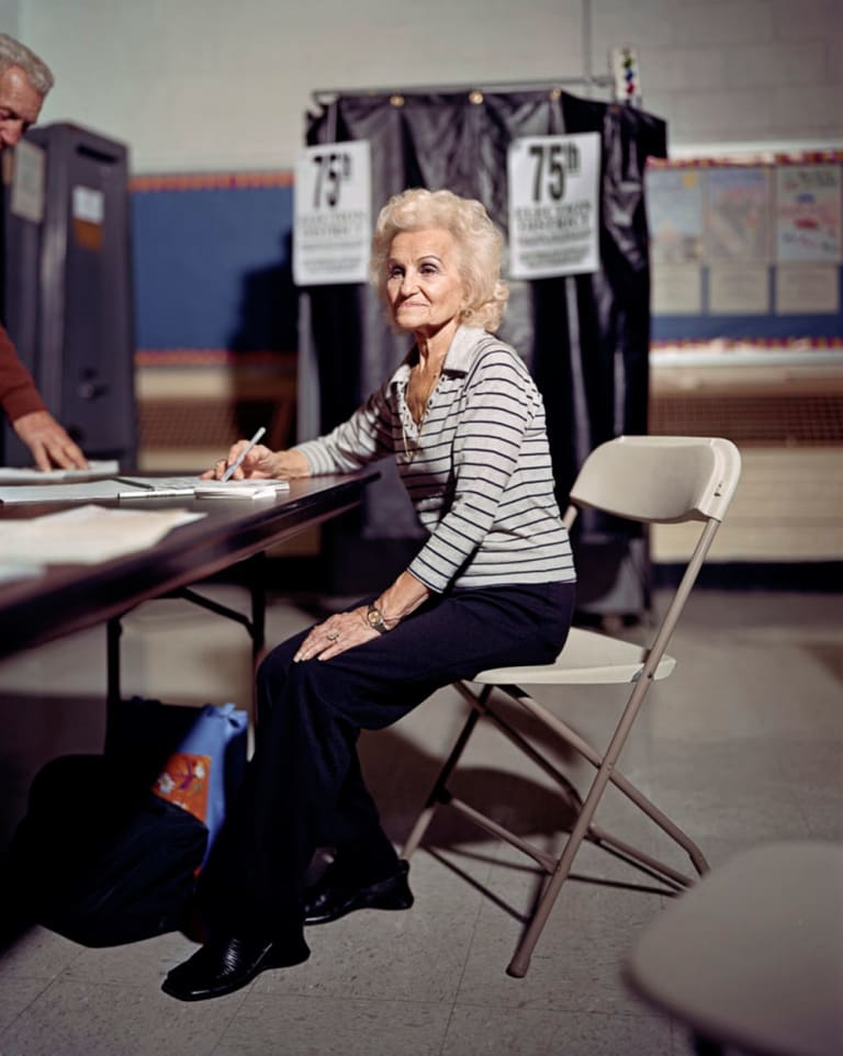 An old lady sitting in a chair and signing or taking notes.