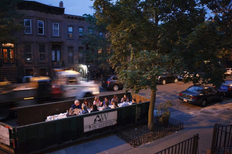 Group of people sitting down and talking while truck passes by.