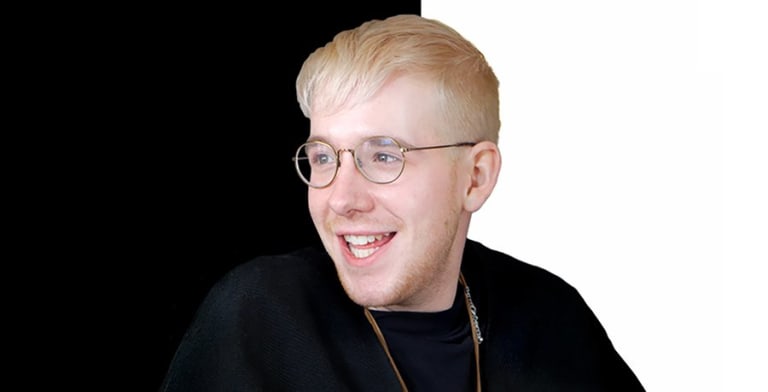 A blonde man with glasses smiling in front of a black and white bisected background.