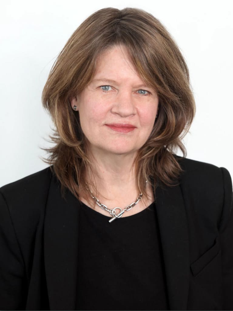 An older woman wearing all black, looking directly at the camera and half-smiling.