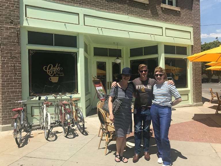 There are 2 women and one male posing for a picture in front of Cafe Sue le lot.