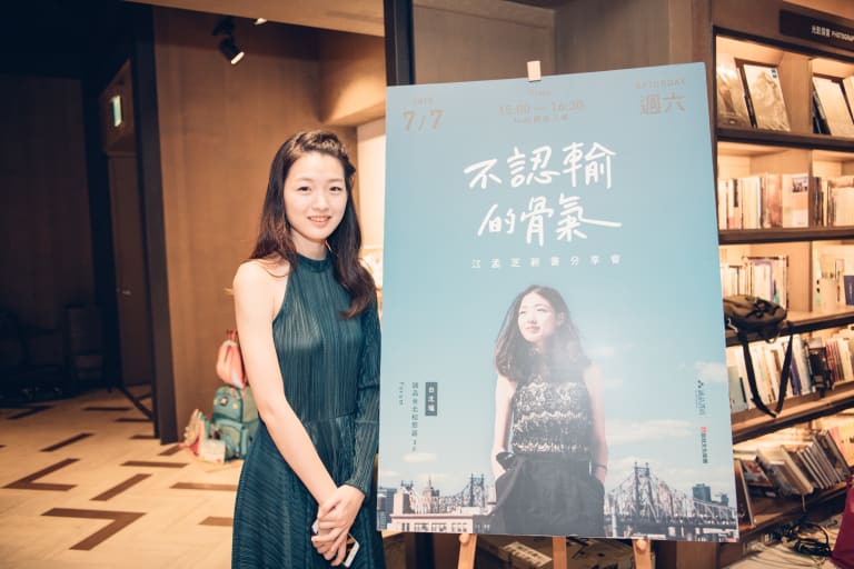 MengChih standing in front of a poster of her book cover in a bookstore.
