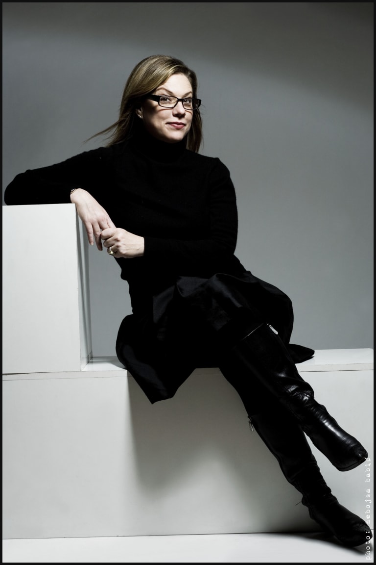 <p "="">A color photograph of a woman dressed in black and sitting on a white platform.
