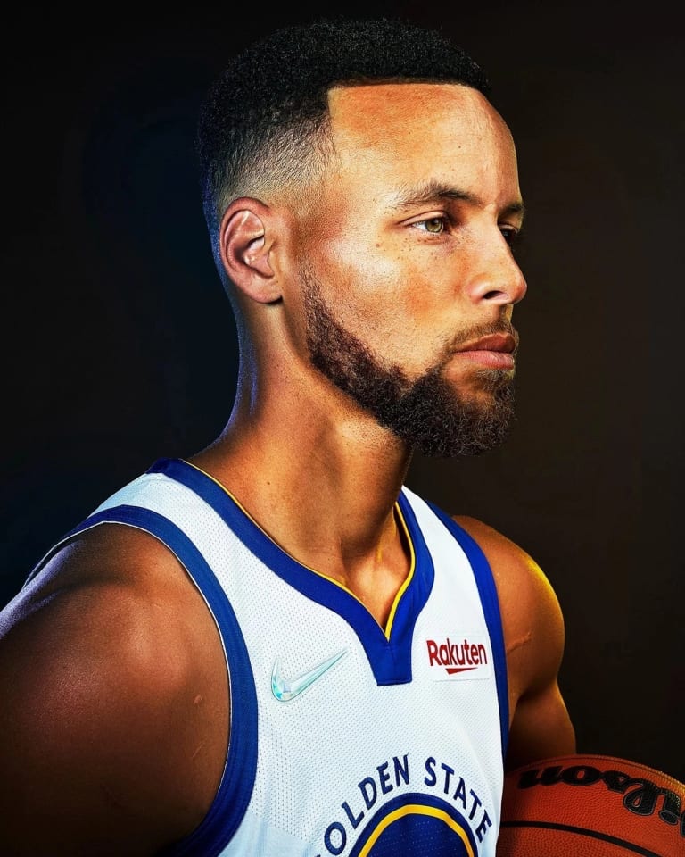 A studio portrait of basketball player Steph Curry. He is holding a basketball and facing the right of the frame.