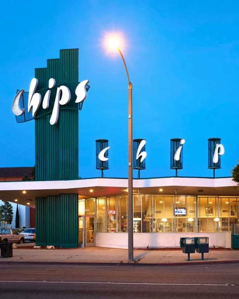 A photograph of the exterior of the Chips Restaurant in Los Angeles, CA, which features a tall, dark green column that bears the name of the restaurant in white letters, and a single story dinning room. 