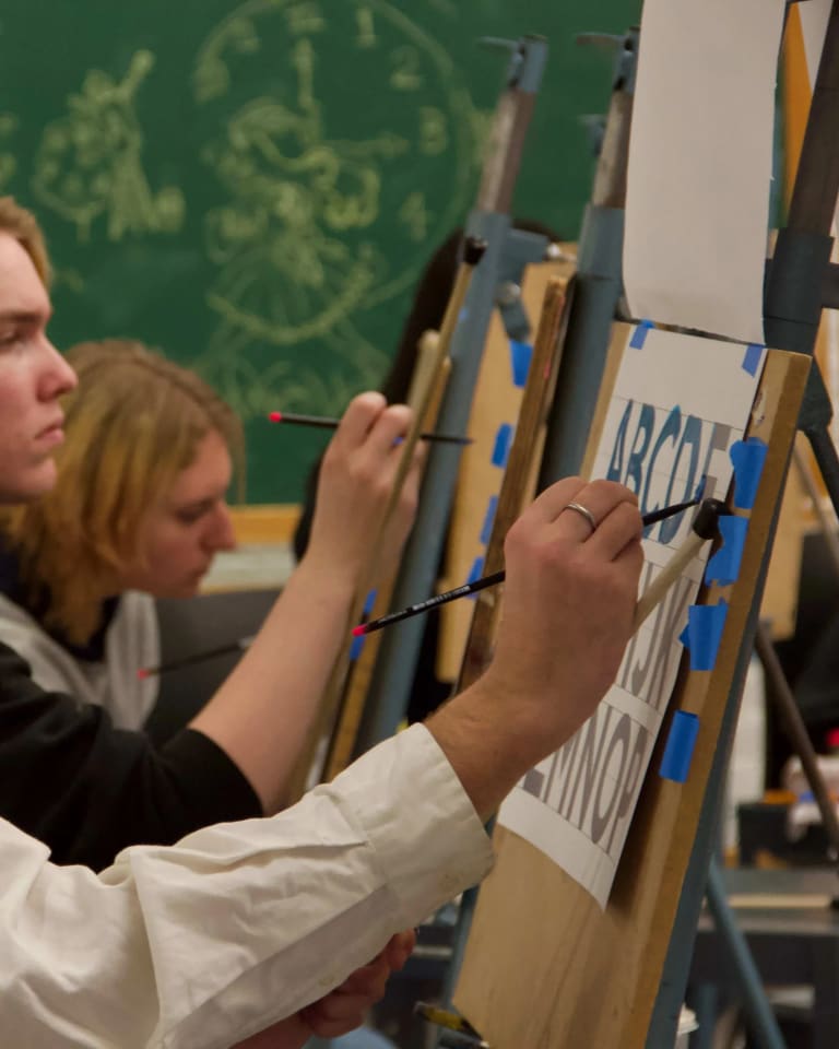 Three students tracing letters with paint as part of the Hand Lettering and Sign Painting spring workshop.