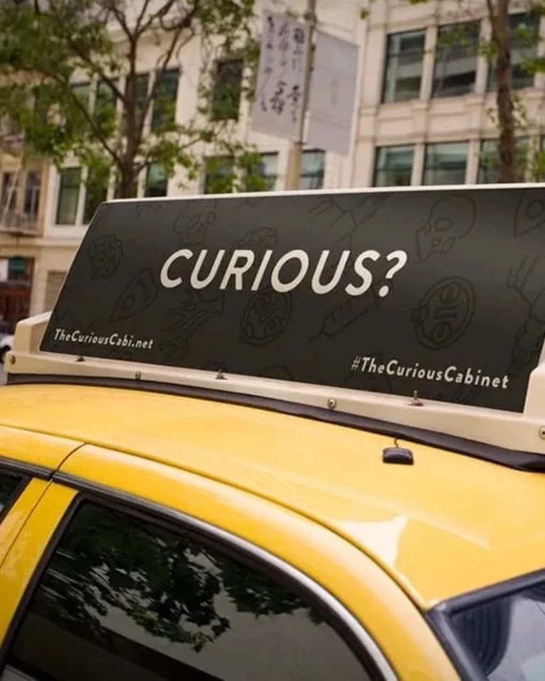 A closeup of a taxi top ad that says "Curious?" in white all caps text on a solid black background