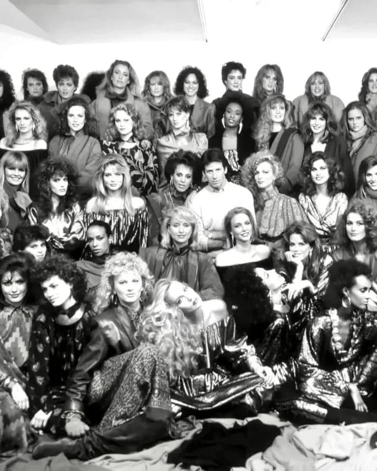 A group of female fashion models posing for a group portrait, with fashion designer Calvin Klein at the center. 