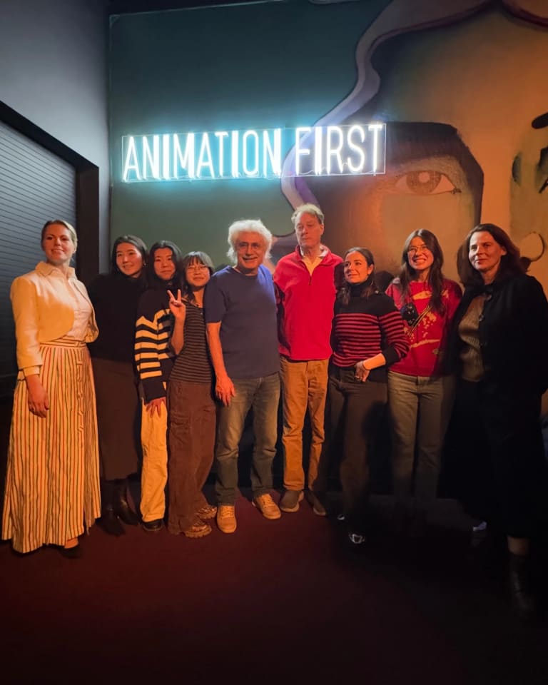 Nine people standing in front of a neon sign that says "Animation First"