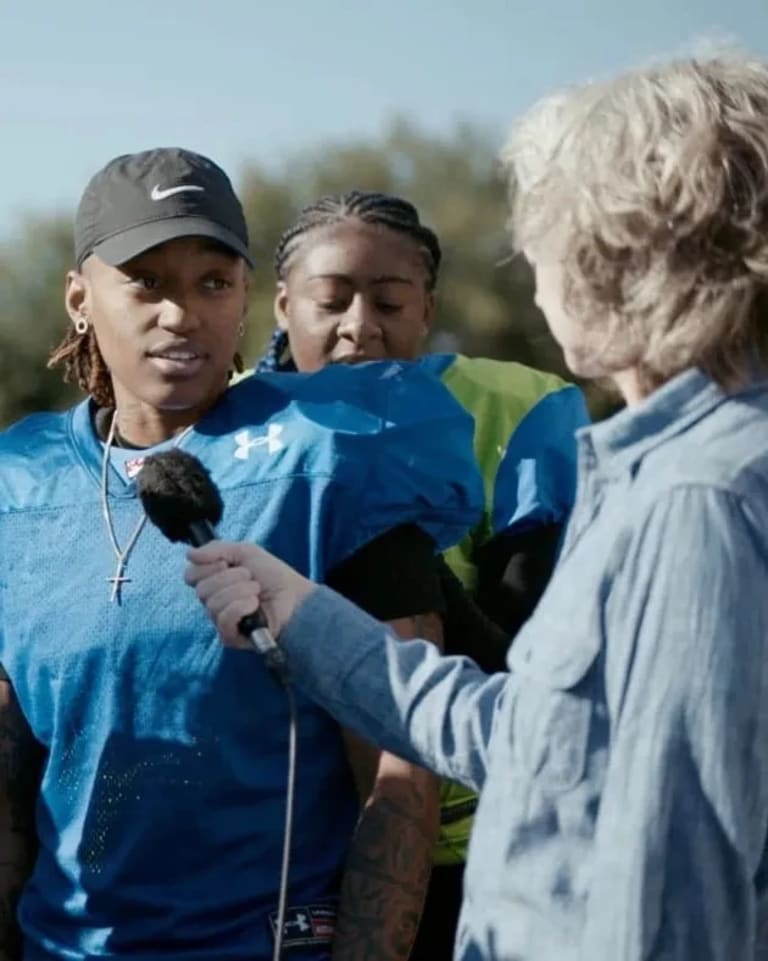 A video still featuring several teammates on a women's football team speaking with a woman who is holding a microphone out to them.