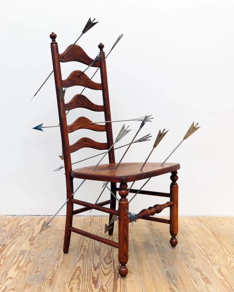 Sculpture consisting of a wooden chair with nine steel arrows piercing its seat and back