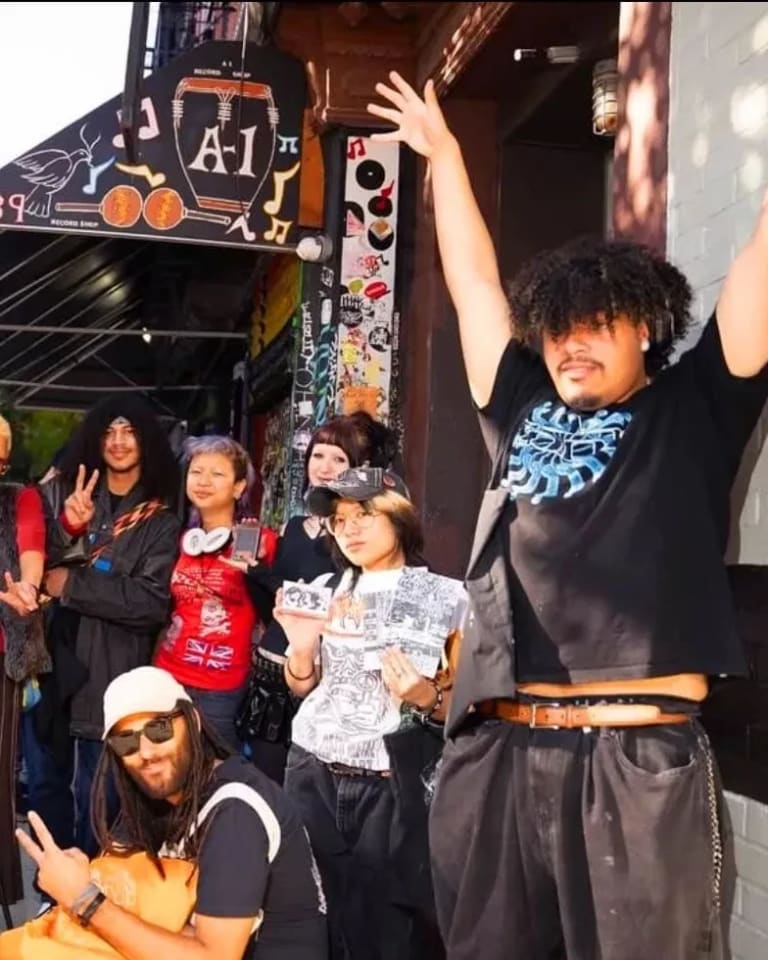 A group of students stand together pose, raise their arms and drop peace signs while smiling at the camera.