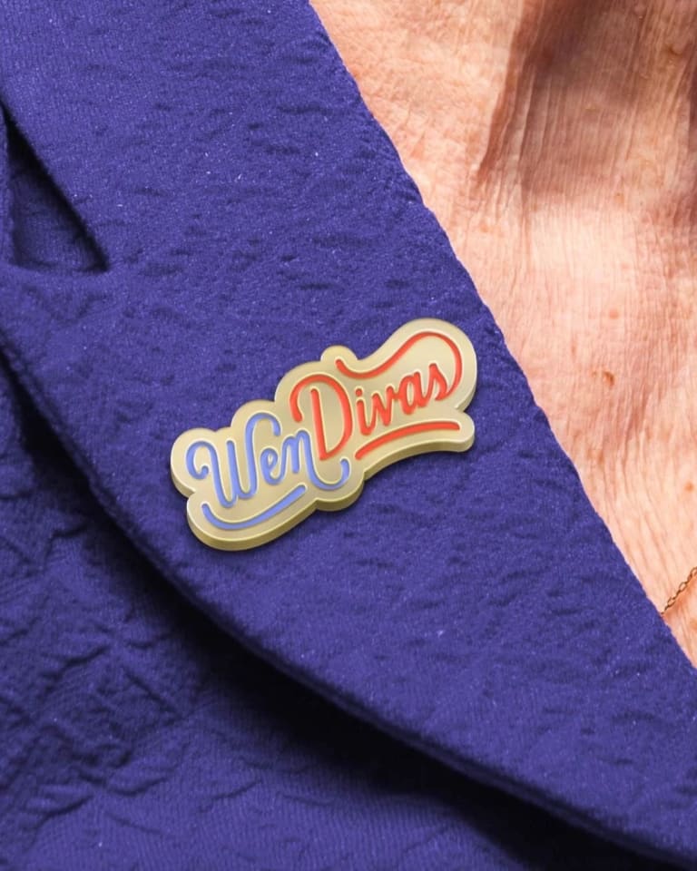 A woman wearing a purple dress with a custom made pin that reads "Wen Divas" pinned to it.