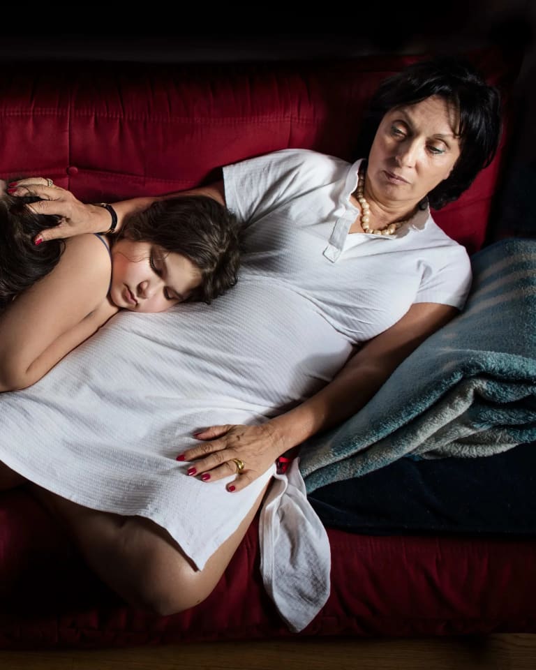 Three people, from three different generations, lying on top each other, together on a red fabric couch. 