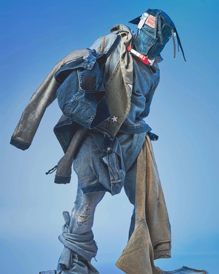 A studio fashion portrait of someone in an all-denim blue outfit and wearing a mask made of denim.