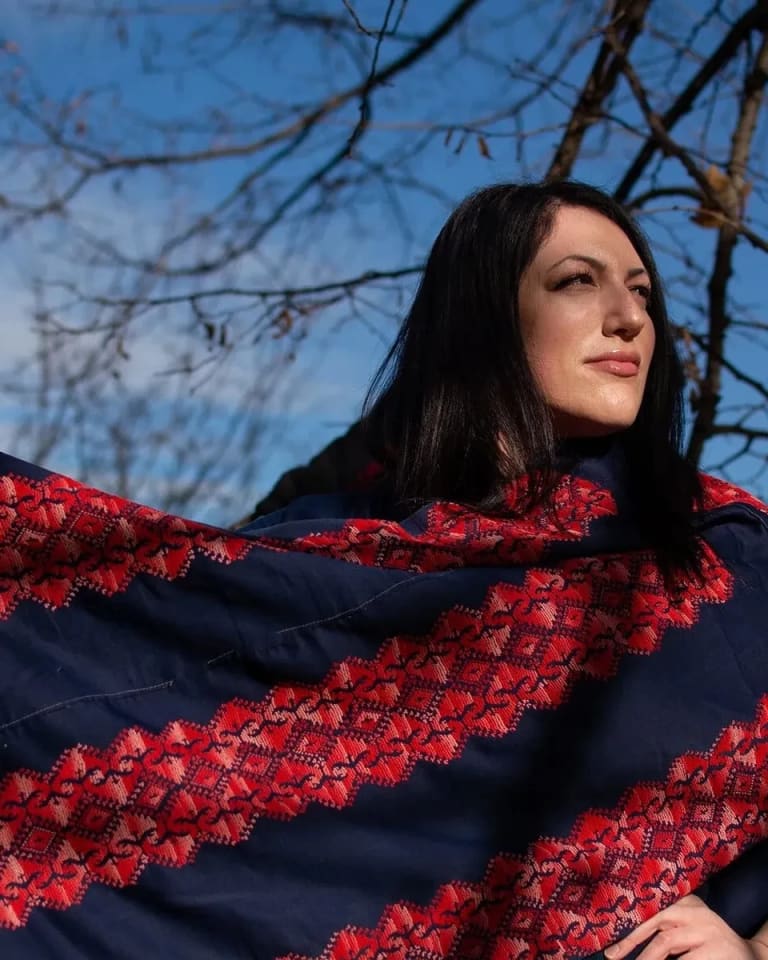 Wafa Ghnaim wearing a piece of Tatreez embroidery with red and blue colors, standing outside