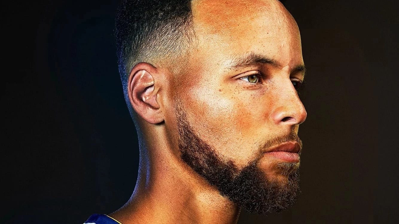 A studio portrait of basketball player Steph Curry. He is holding a basketball and facing the right of the frame.