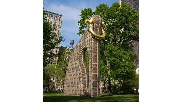 This picture contains some sort of structure surrounded by trees, people standing, and buildings