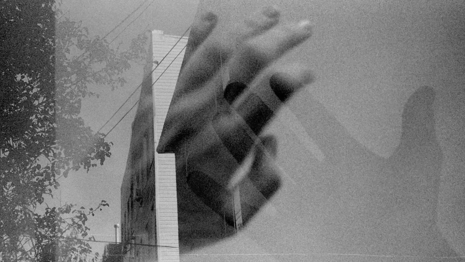 Black and white photo of two hands transposed over an apartment building with trees and power lines.