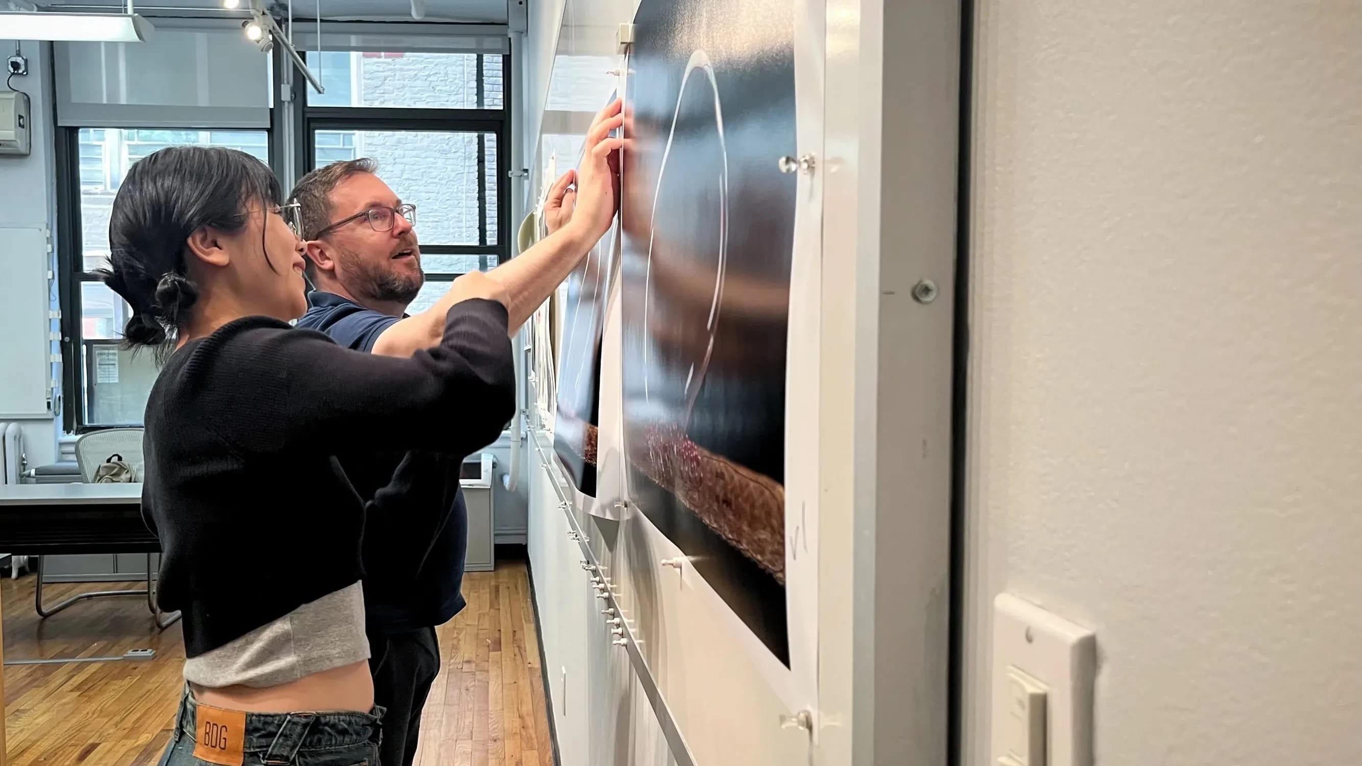 a student and professor examine a photo print that hangs on a wall.