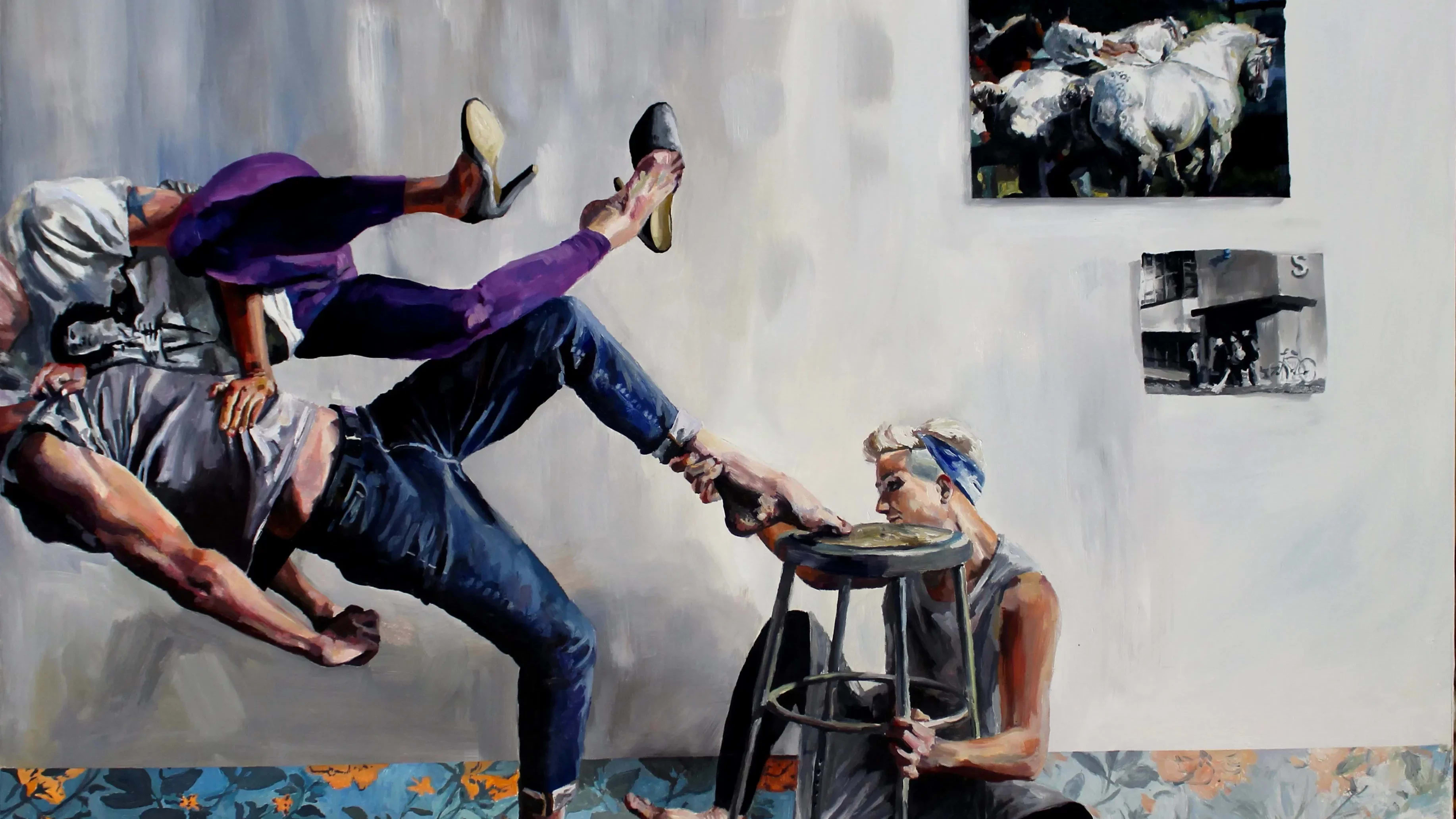 A painting of a seated figure holding on to the feet of a dancer in a grey room with paintings on the wall and a colorful floral carpet.