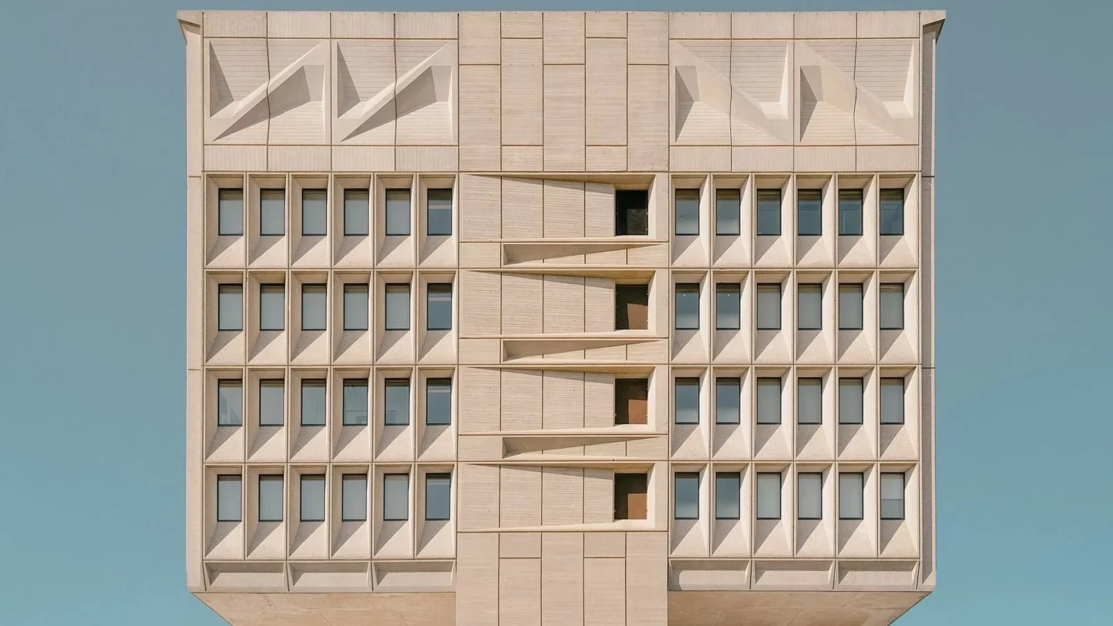 architectural color photo of a large square concrete building against a blue sky.