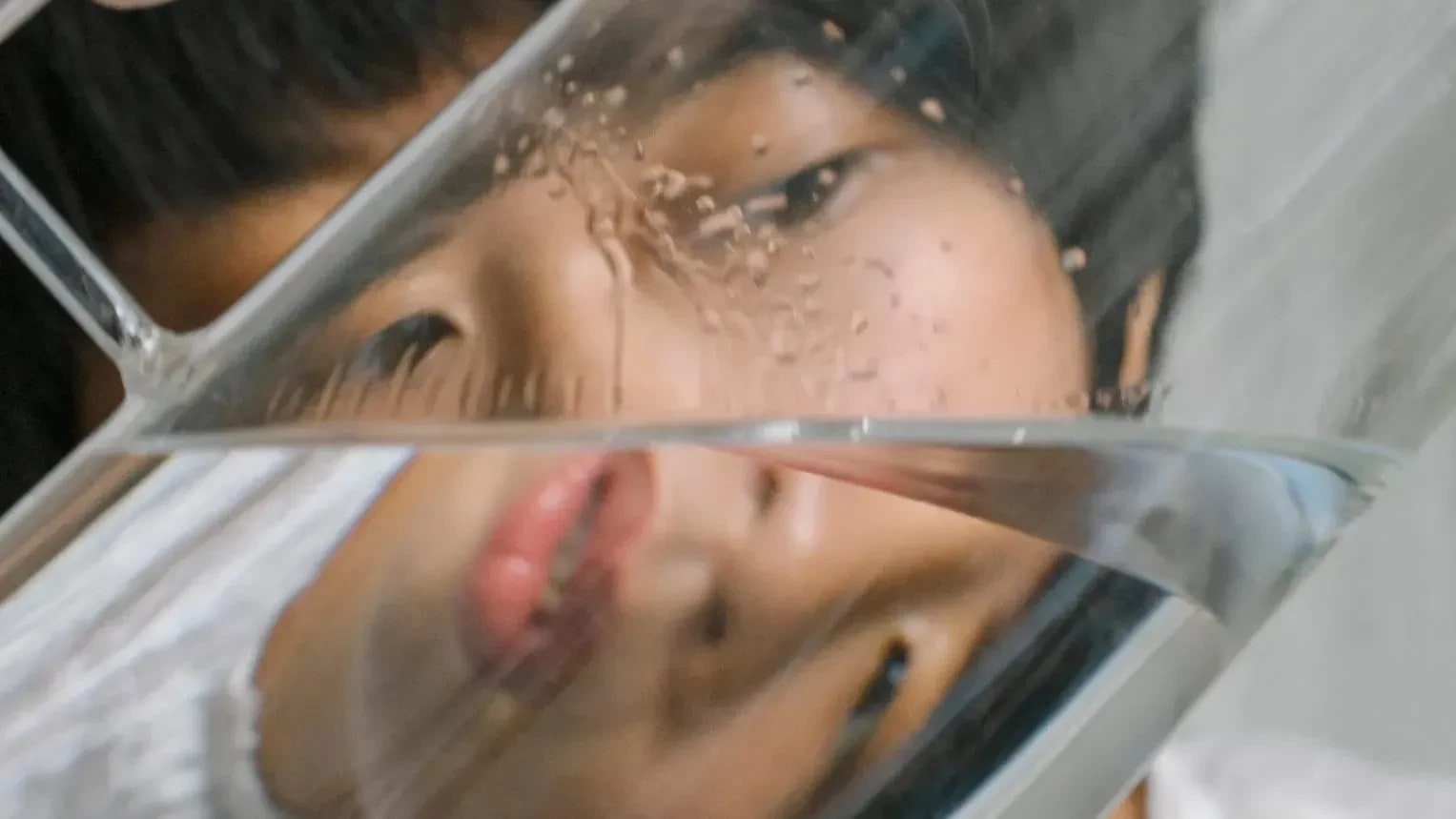 Self-portrait of a woman photographed through a half-empty pitcher, distorting the face.