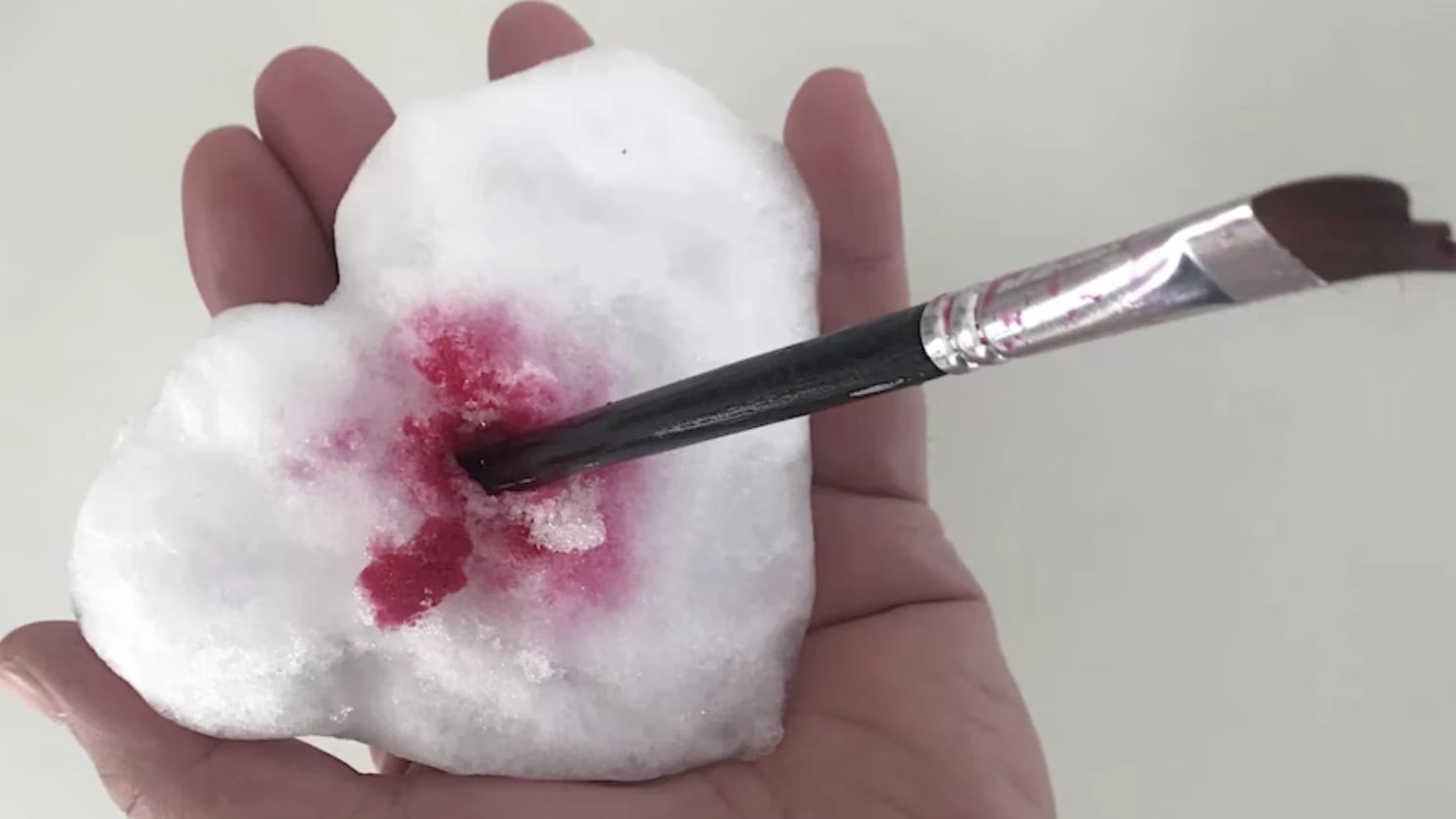 Peter Hristoff's hand with a snow heart pierced with a paint brush and red paint