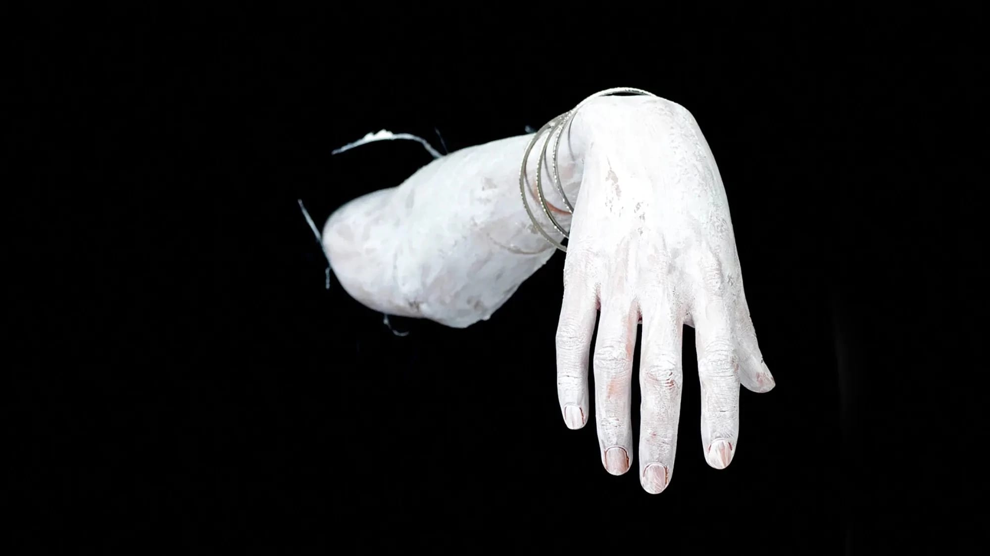 A hand and forearm emerging from darkness, covered with white paint.