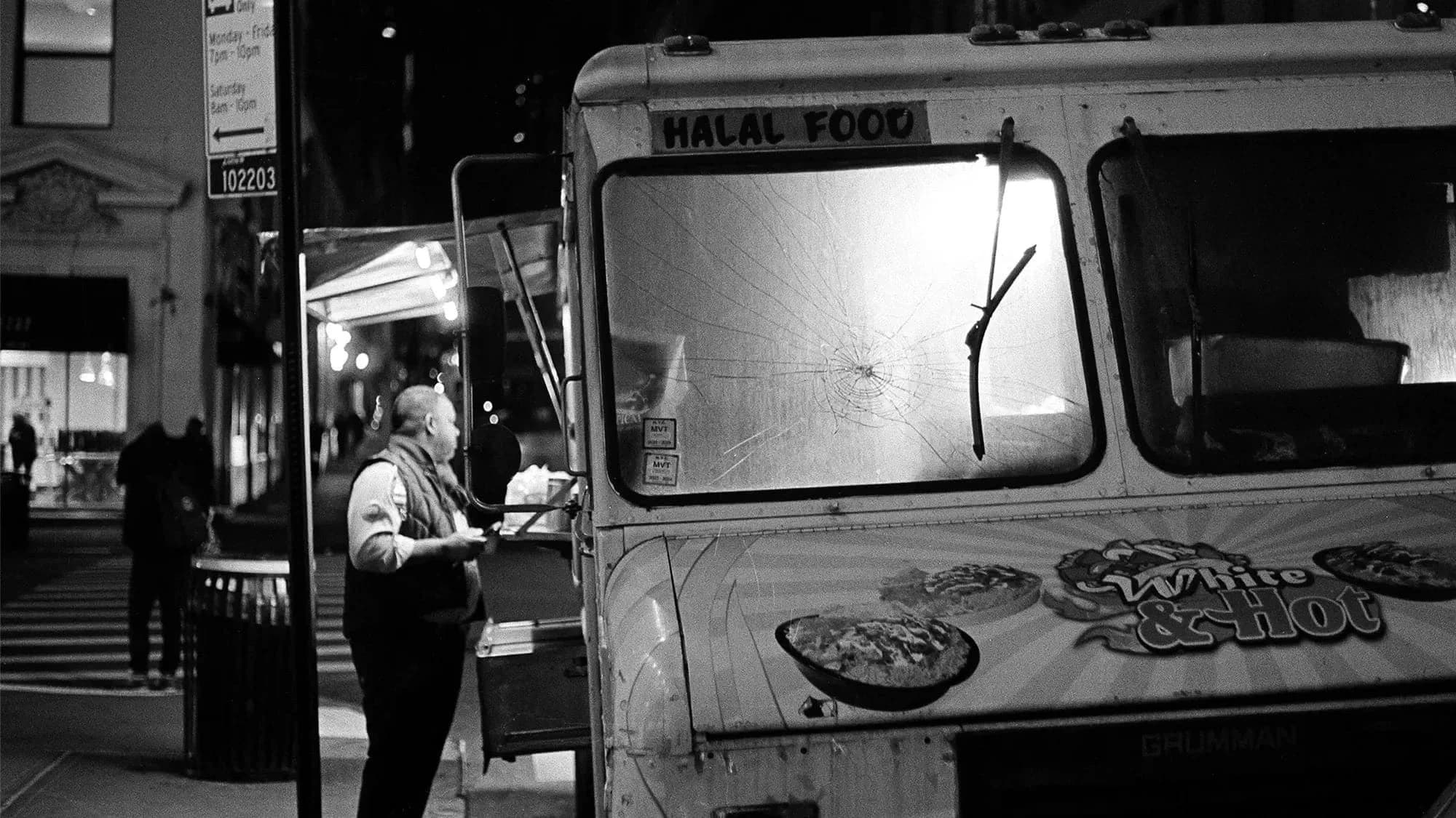A man stands in front of a food truck at night, buying food.