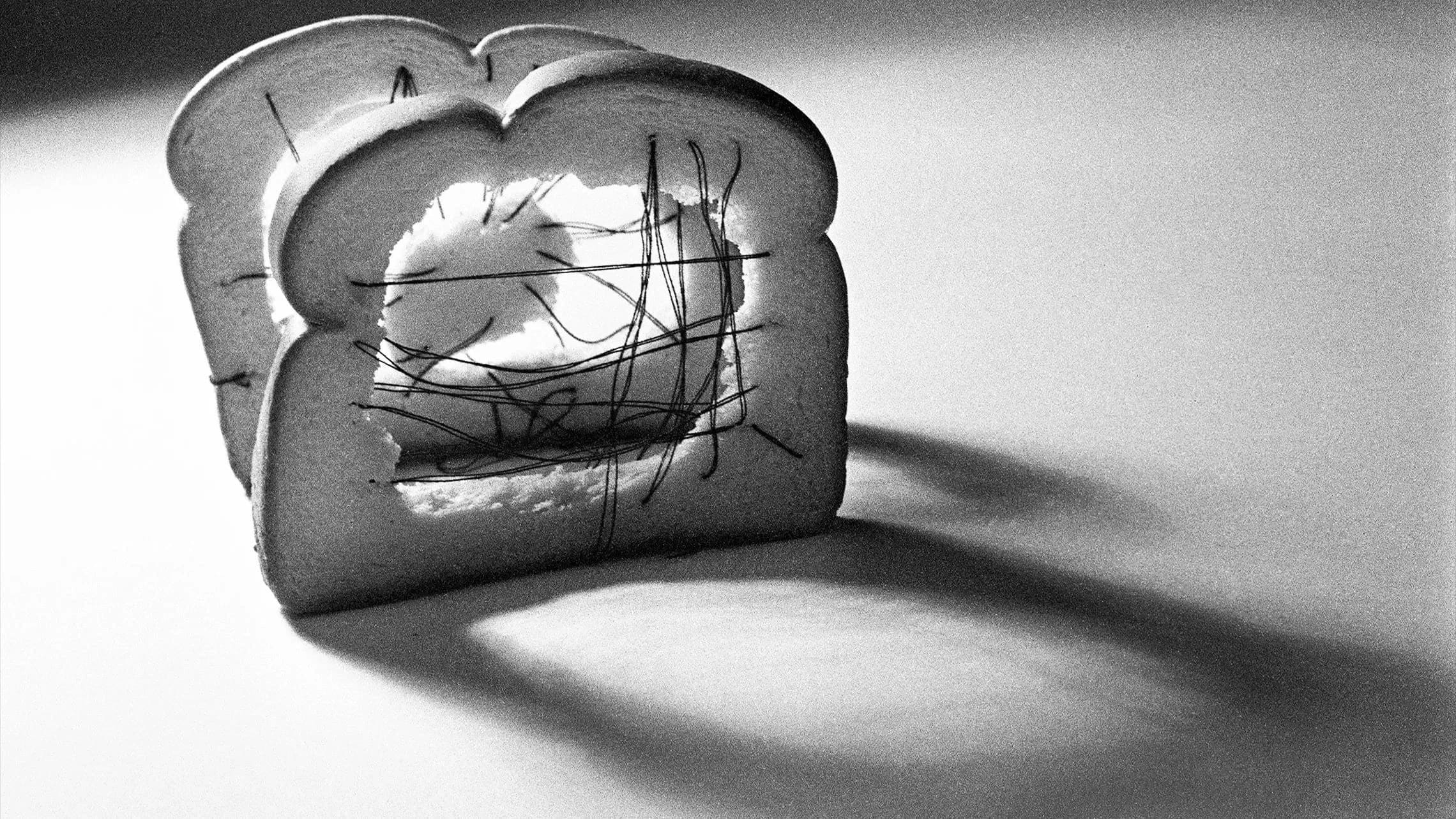 A black and white photo of two slices of bread sewn with thread.