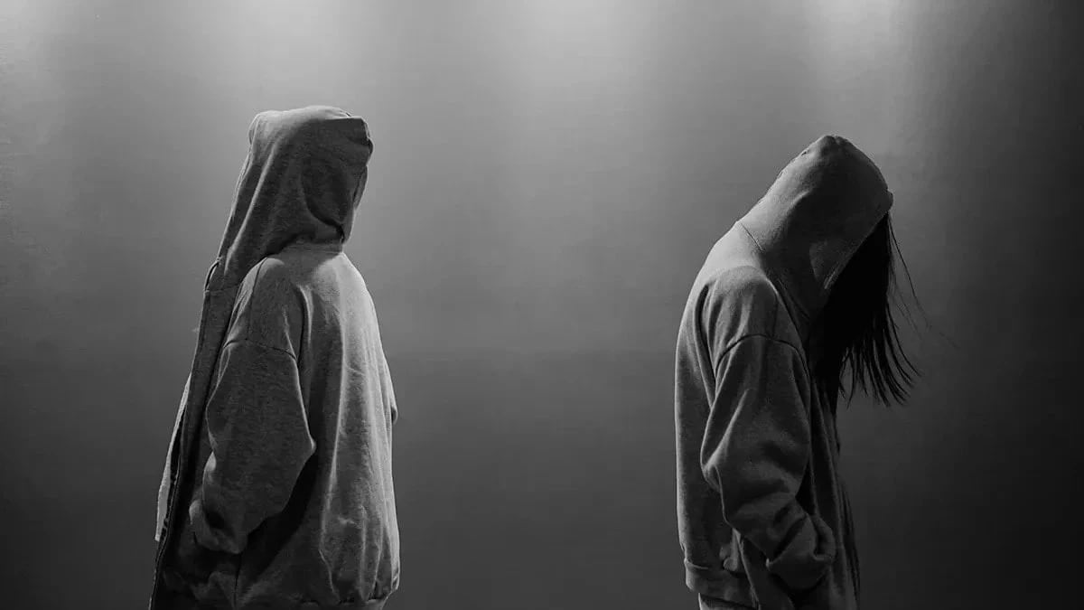 A black and white photo of two people wearing hoodies facing opposite of each other
