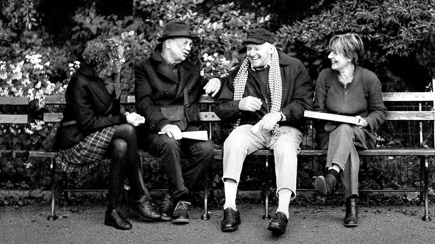 Four friends are sitting shoulder to shoulder in the park talking.