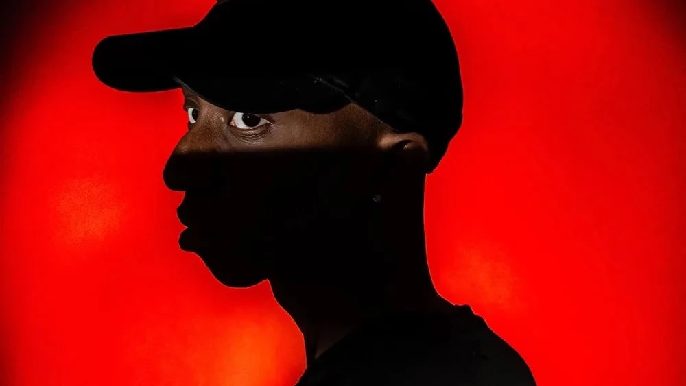 Red backlit circular background, partially silhouetted man with a target on his back