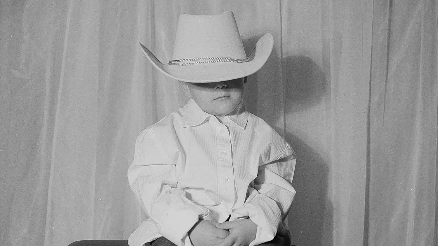 Little boy sitting down wearing a cowboy hat.