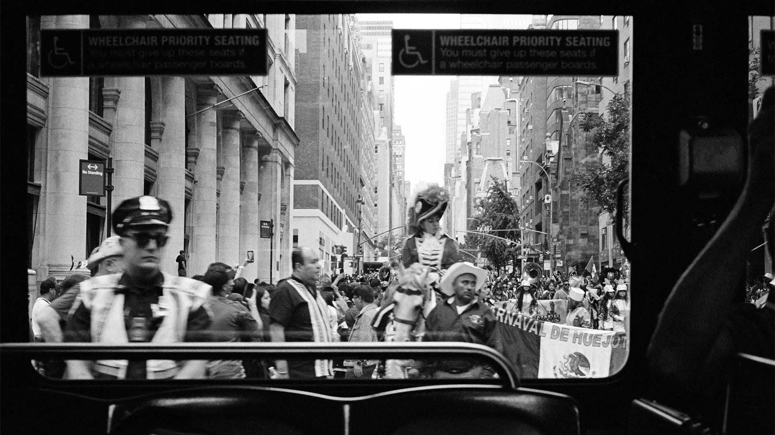 A photo captures the 2023 Hispanic Day Parade on NYC's Fifth Ave, viewed from a bus window.