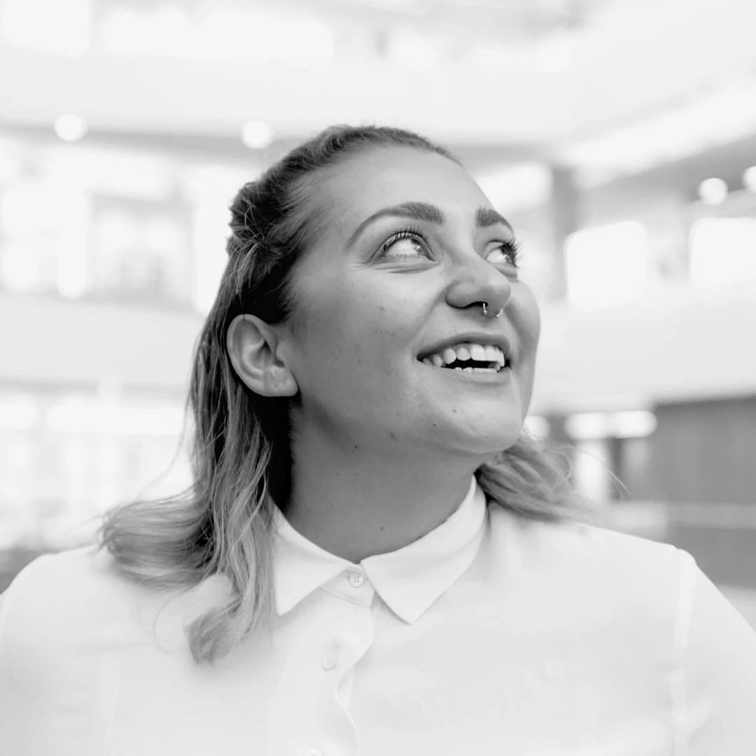 Black and white headshot of Amelia Nash. She is wearing a white button-up blouse, smiling, and looking upwards.