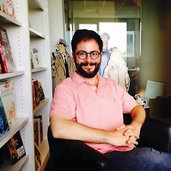 A portrait of Bill Kartalopoulos in an office surrounded by cartoon cut-outs