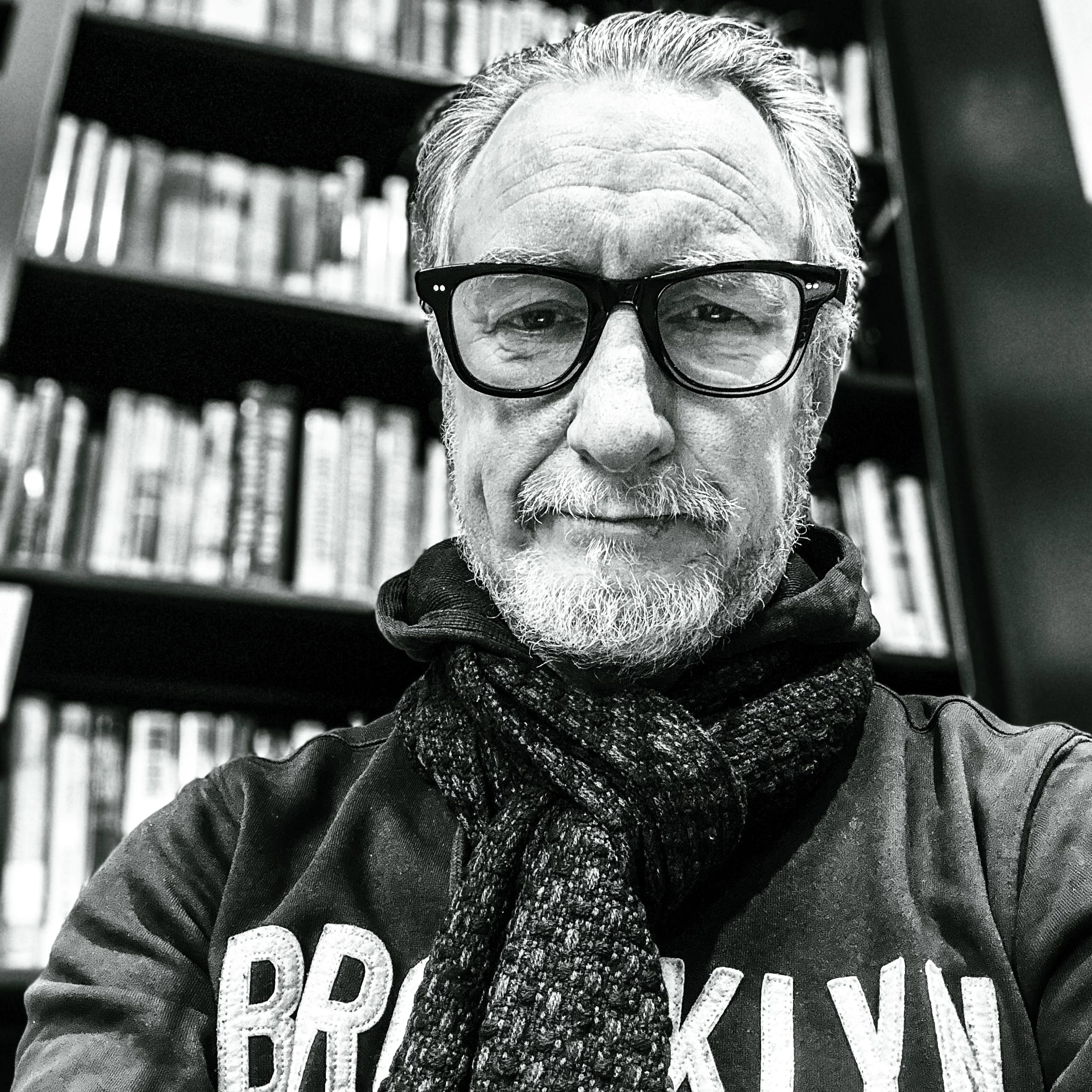 Photo of man with short beard, black-rimmed glasses wearing a Brooklyn hoodie and a scarf.
