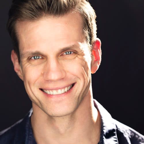 Portrait of Lee Aaron Rosen wearing a dark blue shirt against a dark background