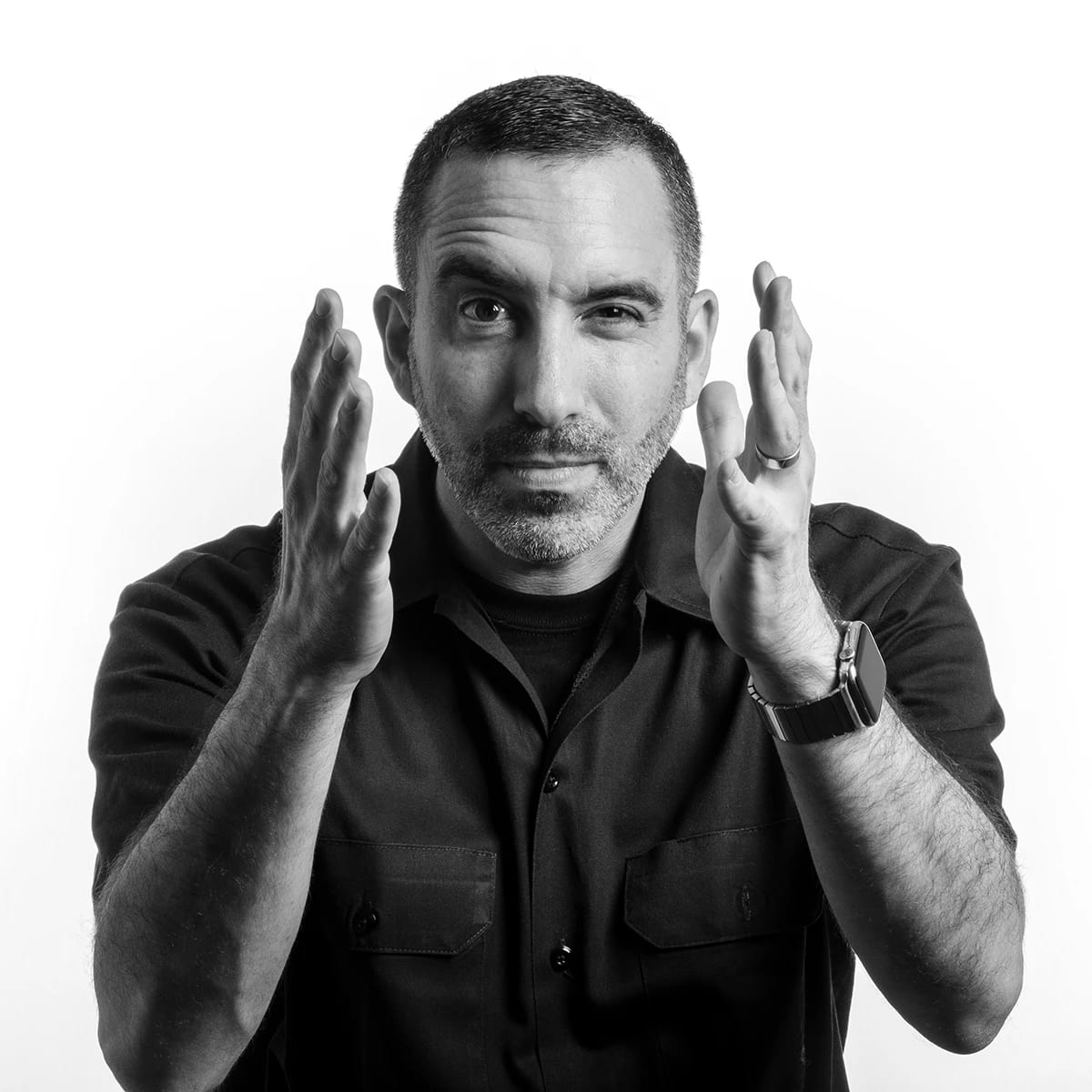 Black and white portrait of a middle-aged man with short dark hair and facial stubble, wearing a dark button-up shirt.