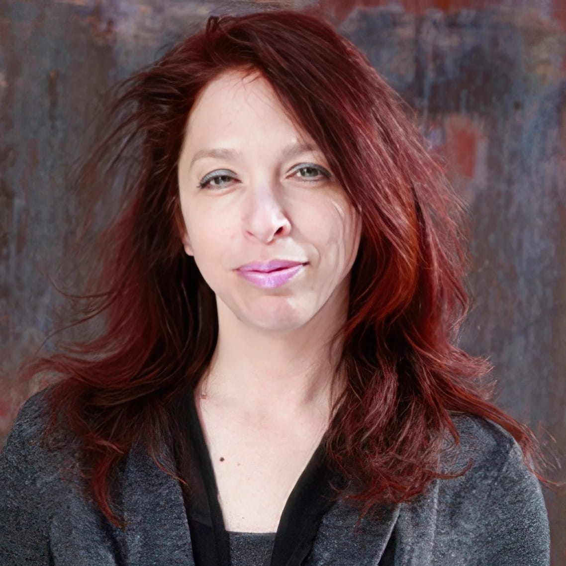 Image of a woman looking at the camera. The woman has red hair and is wearing a gray top.