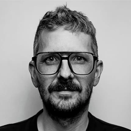 Black and white portrait of man with short hair, glasses, mustache, and black shirt