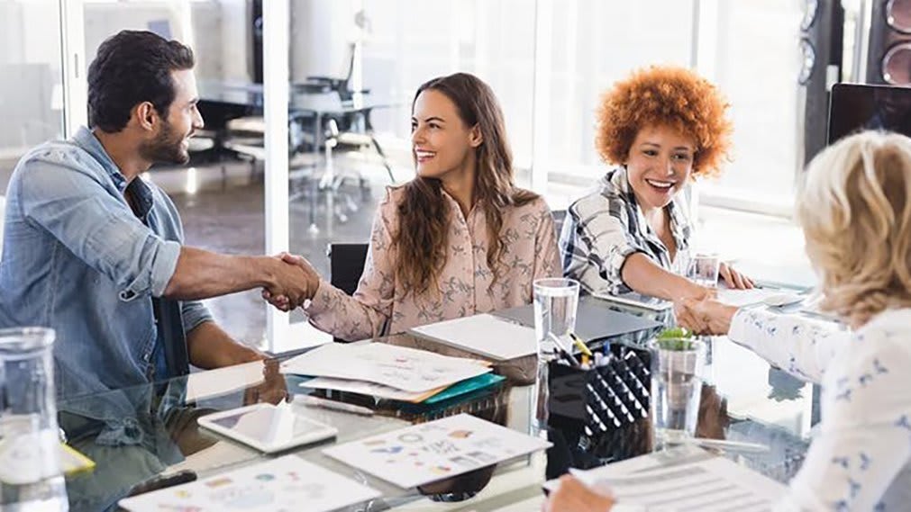 group of people at a conference table shaking hands hello happily