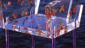 Acrylic clear chair with purple legs sitting in water. The chair has pressed leaves set in the acrylic arms and seat.