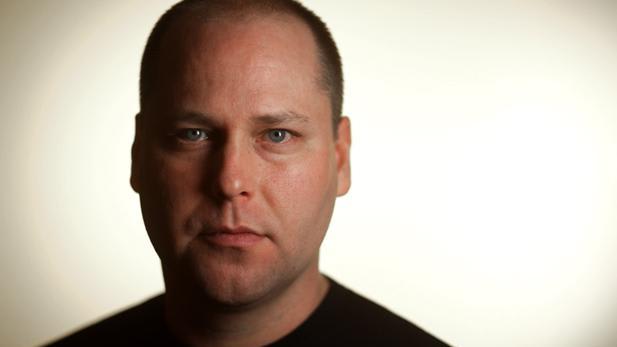 A man with a short haircut and blue eyes looking straight forward.