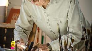 An old man bent over a desk gluing something.