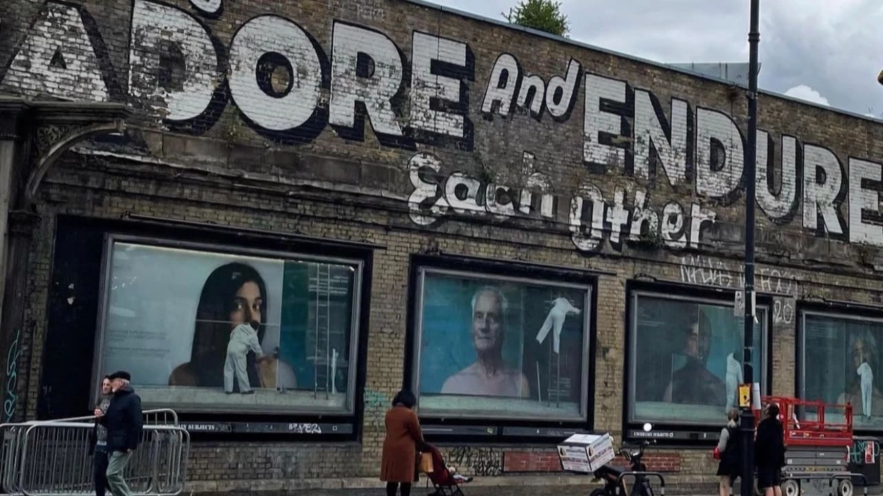 A photo of a building with "adore and endure each other" written above big images of people plastering portraits up on a wall. 